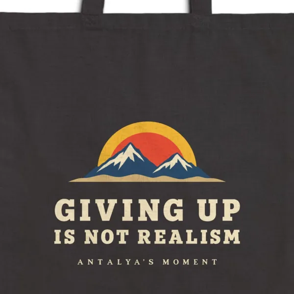 Close-up of the Giving Up Is Not Realism Night design printed on a black canvas tote, with the top seam and handles