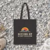 Giving Up Is Not Realism Night design on a black canvas tote, laid flat