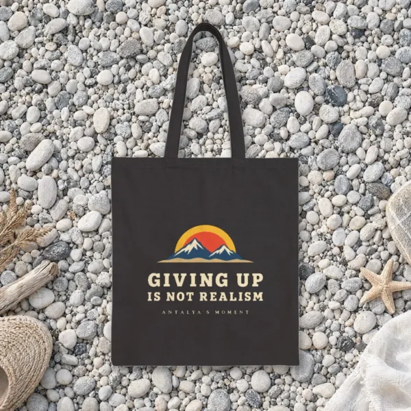 Giving Up Is Not Realism Night design on a black canvas tote, laid flat