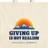 Close-up of the Giving Up Is Not Realism design printed on a natural canvas tote, with the top seam and handles