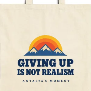 Close-up of the Giving Up Is Not Realism design printed on a natural canvas tote, with the top seam and handles