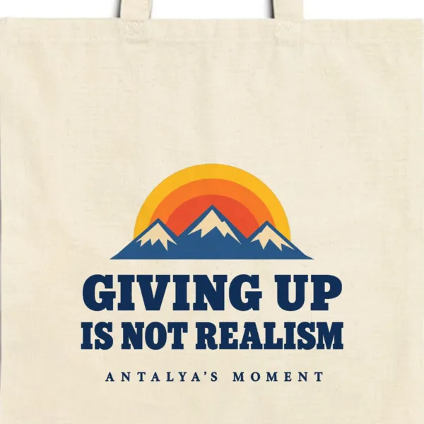Close-up of the Giving Up Is Not Realism design printed on a natural canvas tote, with the top seam and handles